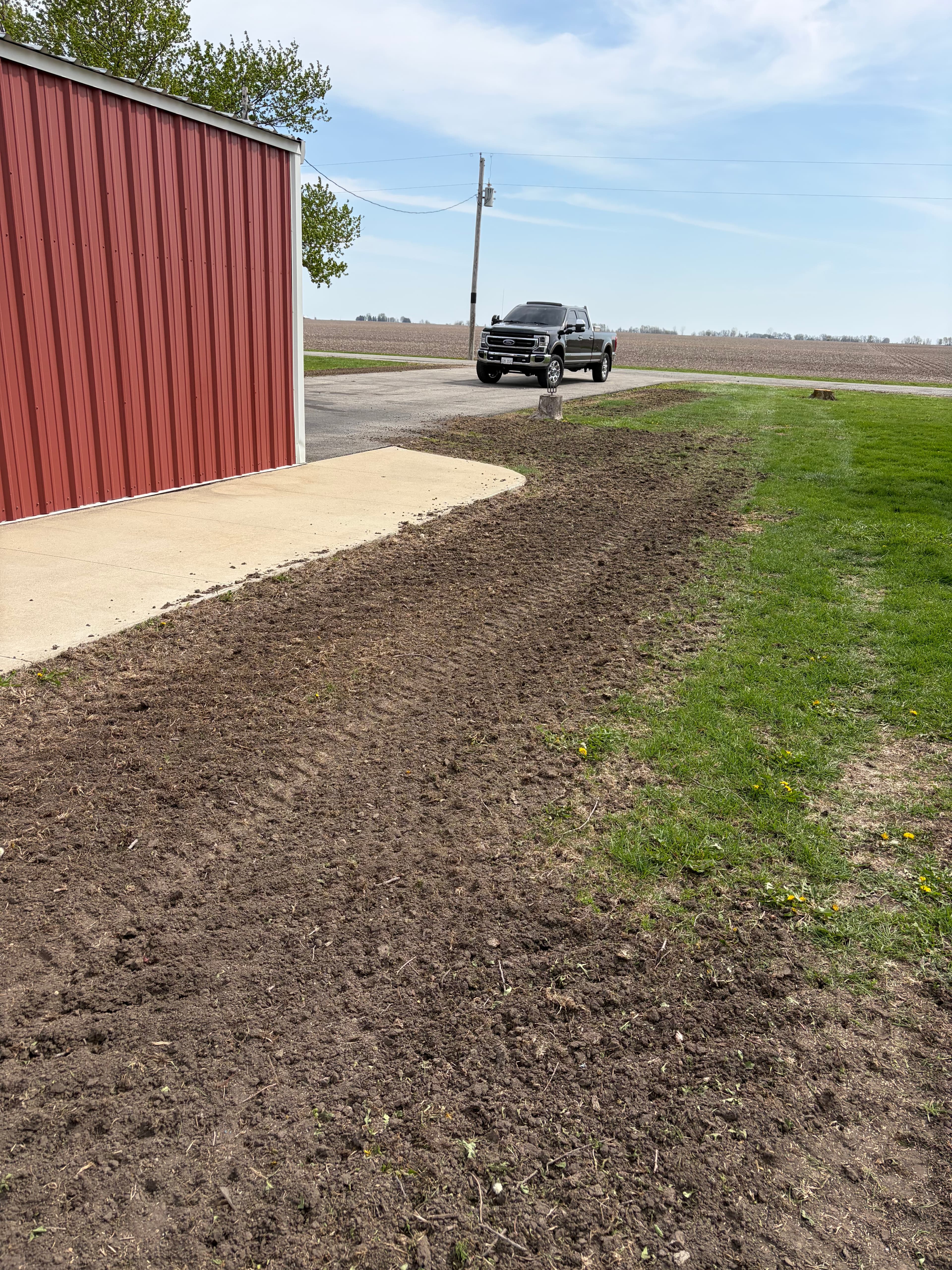 Fresh seedbed and grading work for lawn overseeding near a farm building